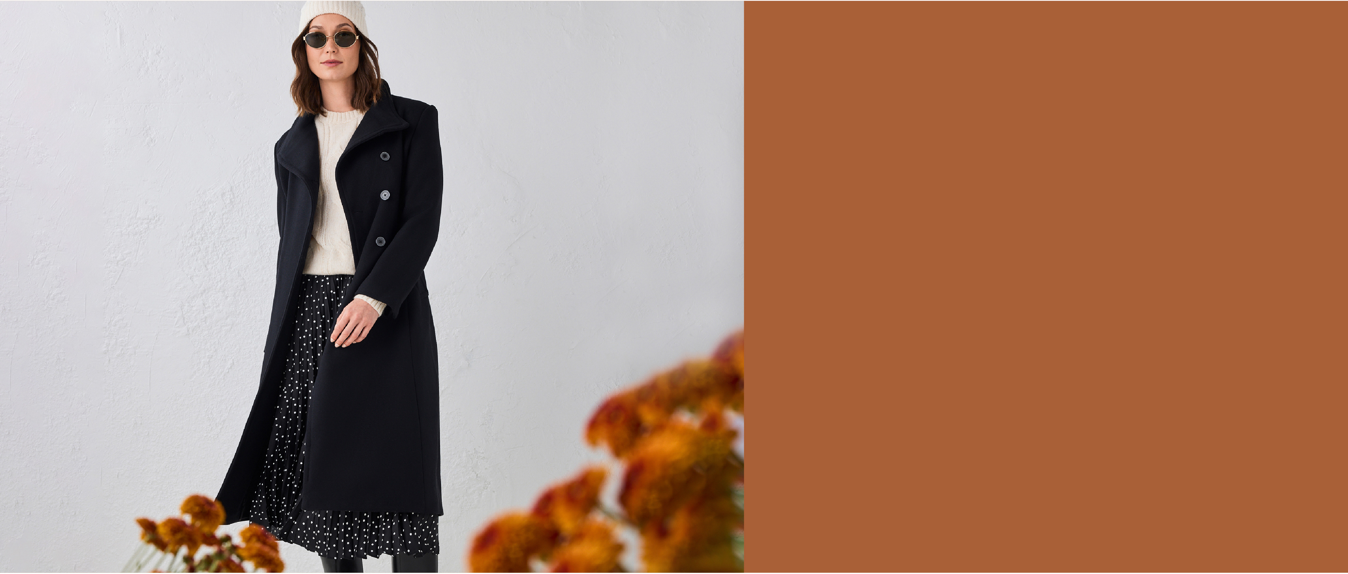 Woman in a black coat, standing against a neutral background with flowers.