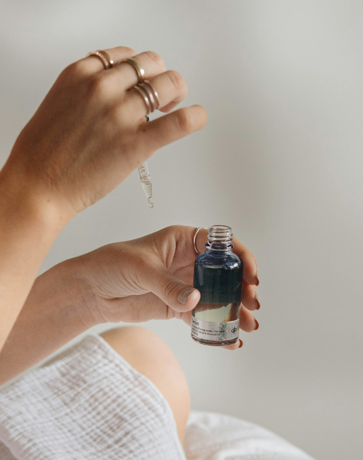 Two hands, one of which is holding a pipette, the other of which is holding a bottle of essential oils