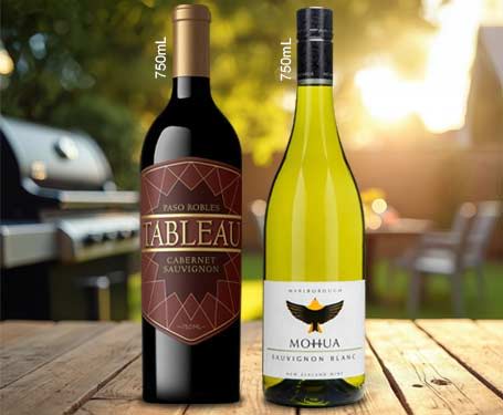 Two wine bottles on a table with a grill and sunset background.