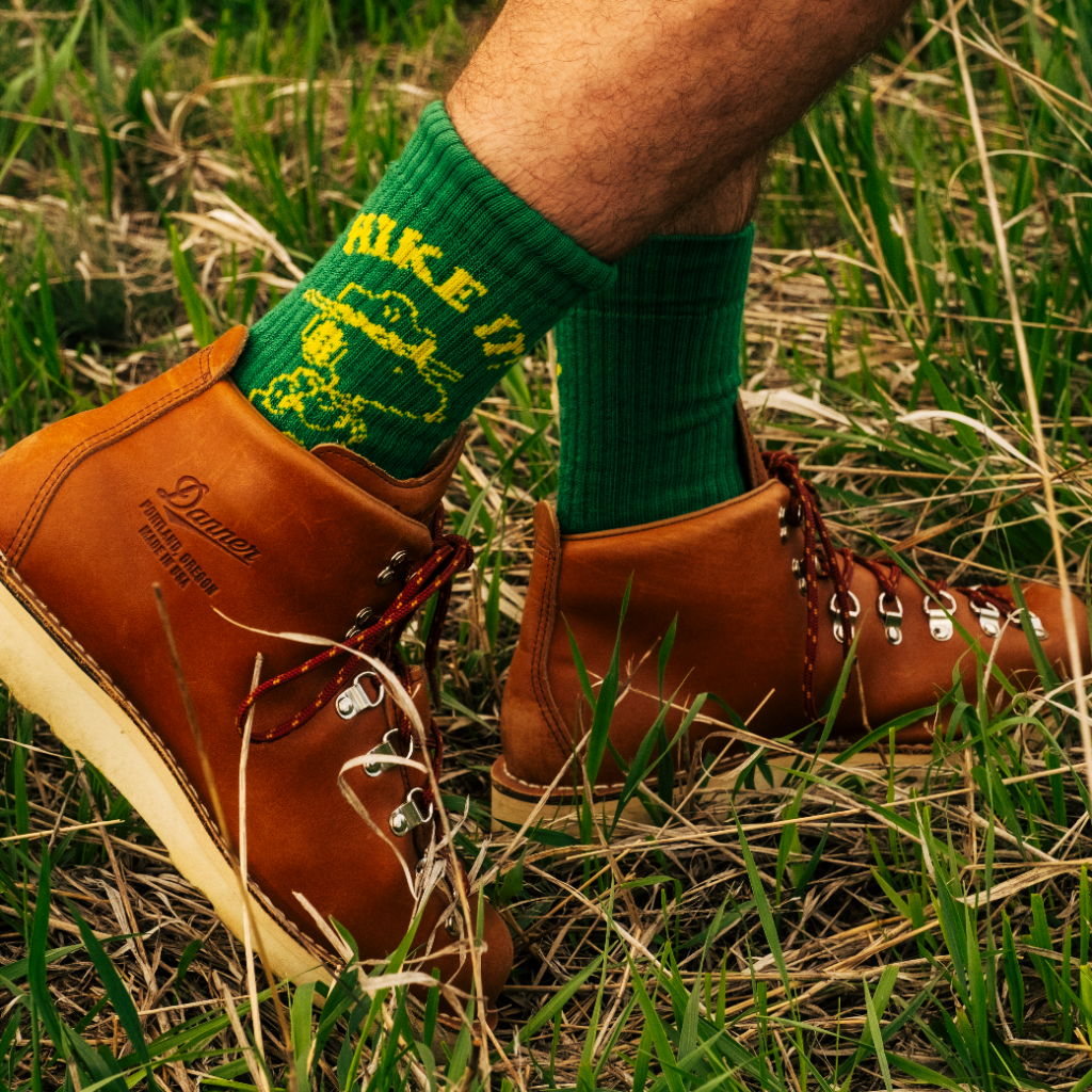 A leg wearing brown boots and green socks in grass.