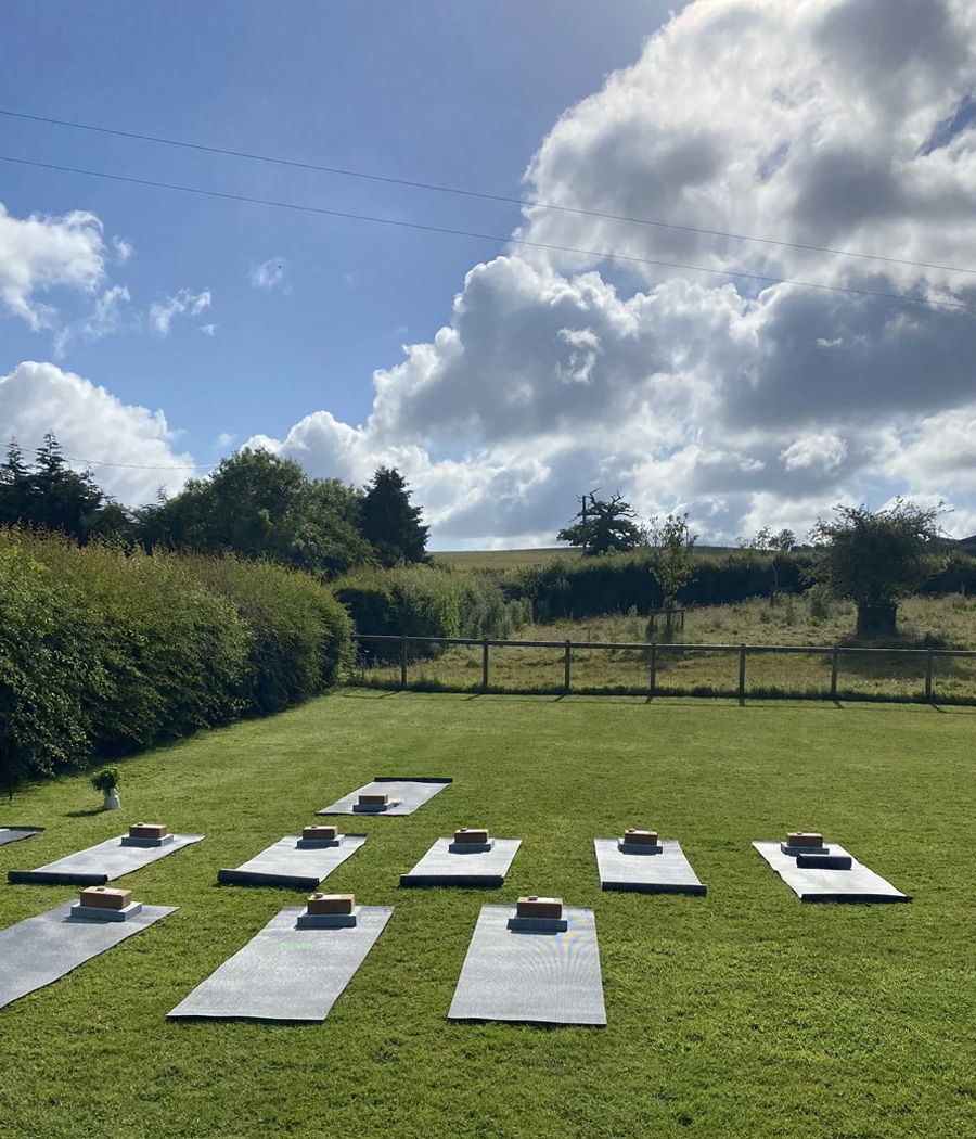 Yoga mats arranged on grass under a blue sky with clouds.