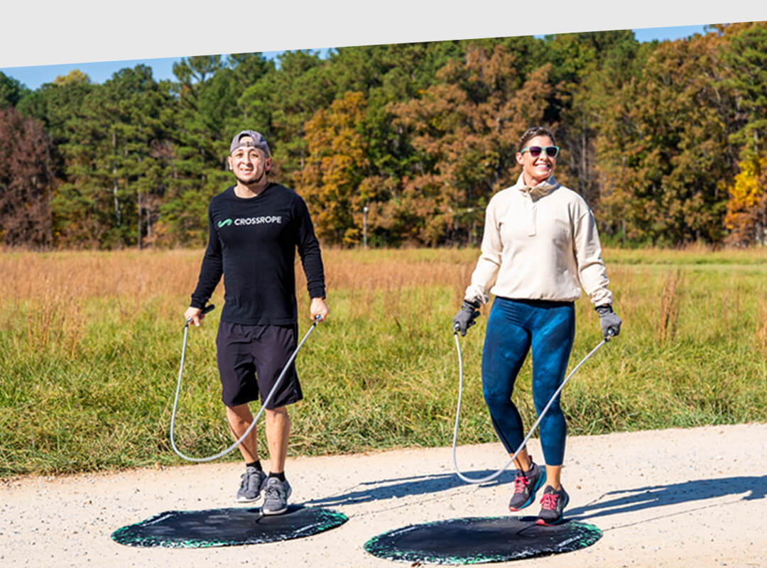 Two people jumping rope on a path in a park with trees in the background