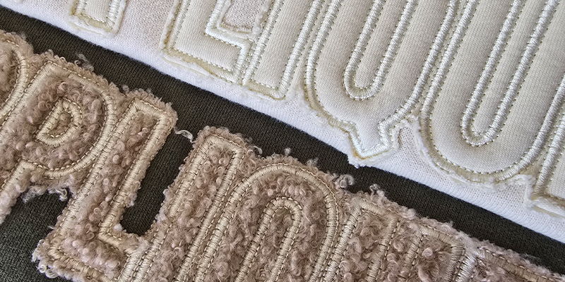 Close-up of appliqué lettering showing textured fabric layers secured with visible stitching creating a raised and dimensional effect
