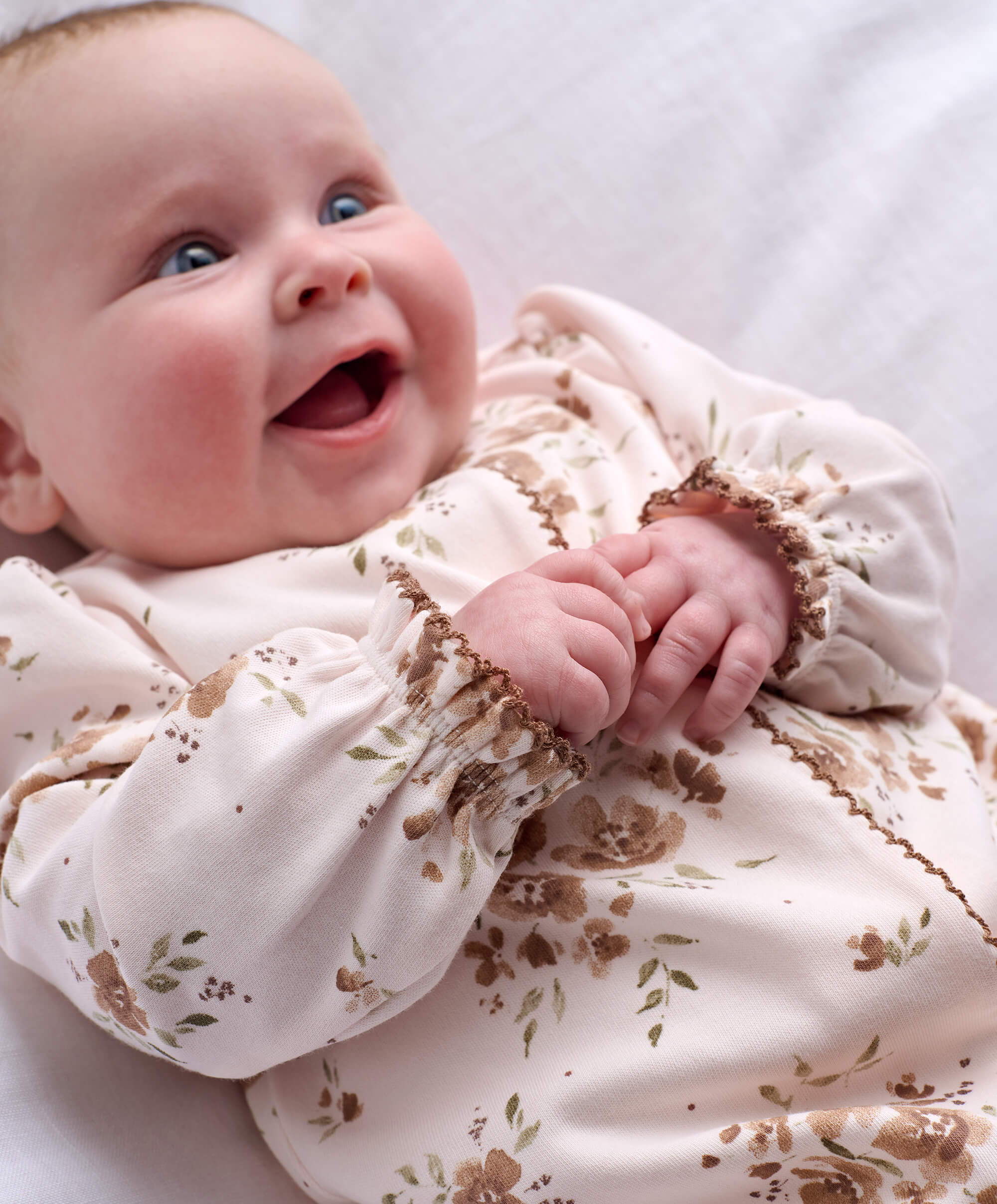 Smiling baby in floral outfit, lying on a soft surface.