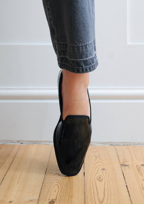 A styled image of a model foot on point wearing the Drogheria Crivellini Patent Venetian Loafer in black.