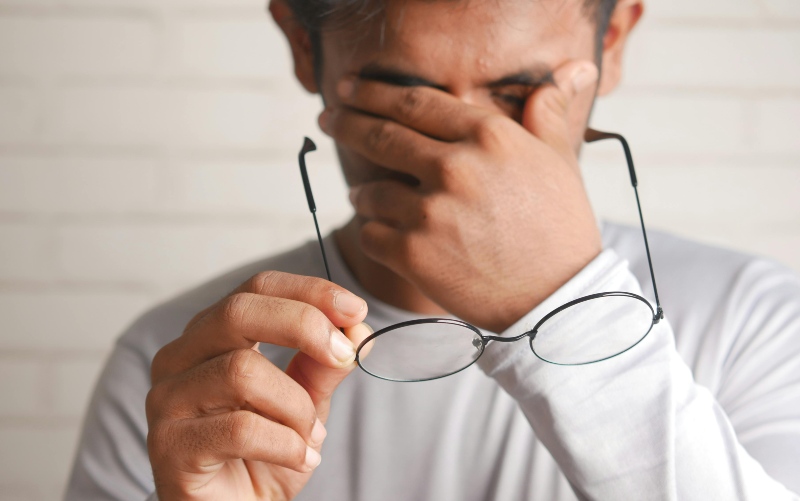 man rubbing eyes due to eye fatigue while holding his glasses