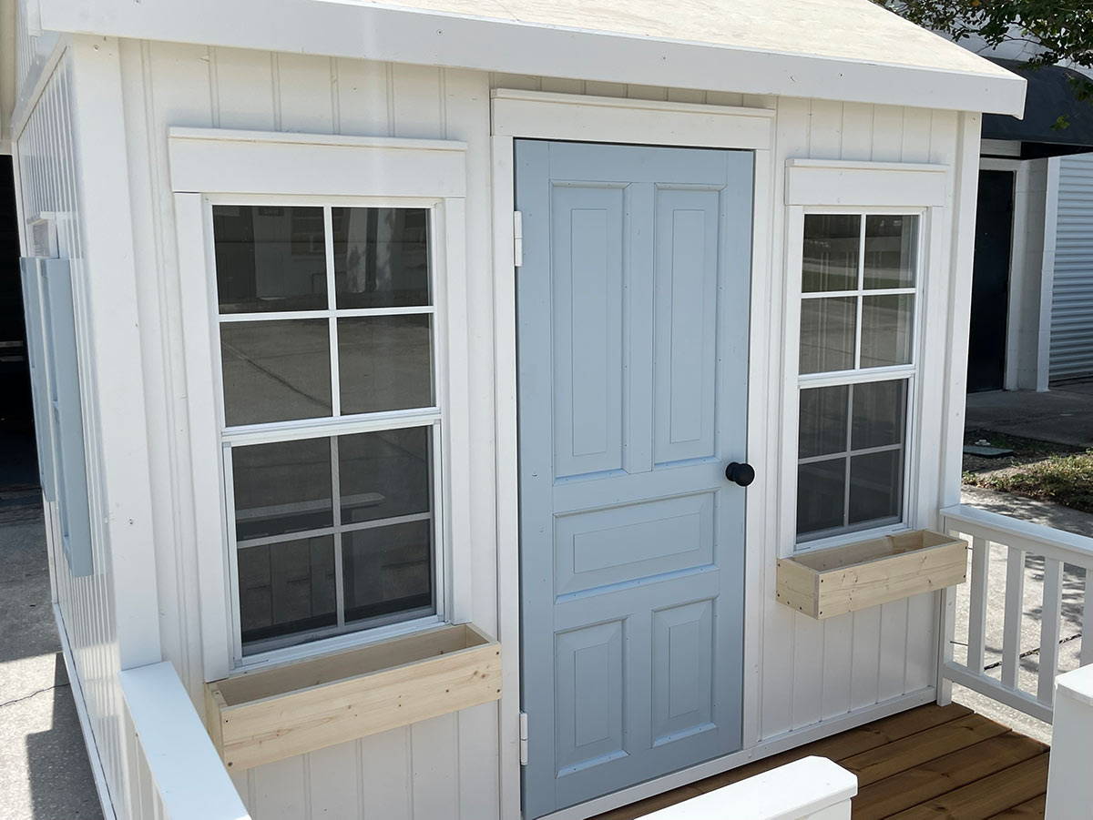 Custom Playhouse from front with blue wooden door and 2 functional windows by WholeWoodPlayhouses