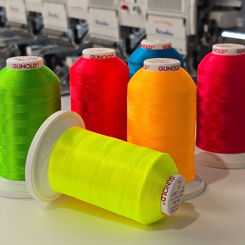 Assorted Gunold embroidery thread cones in neon yellow, red, green and orange arranged on workbench