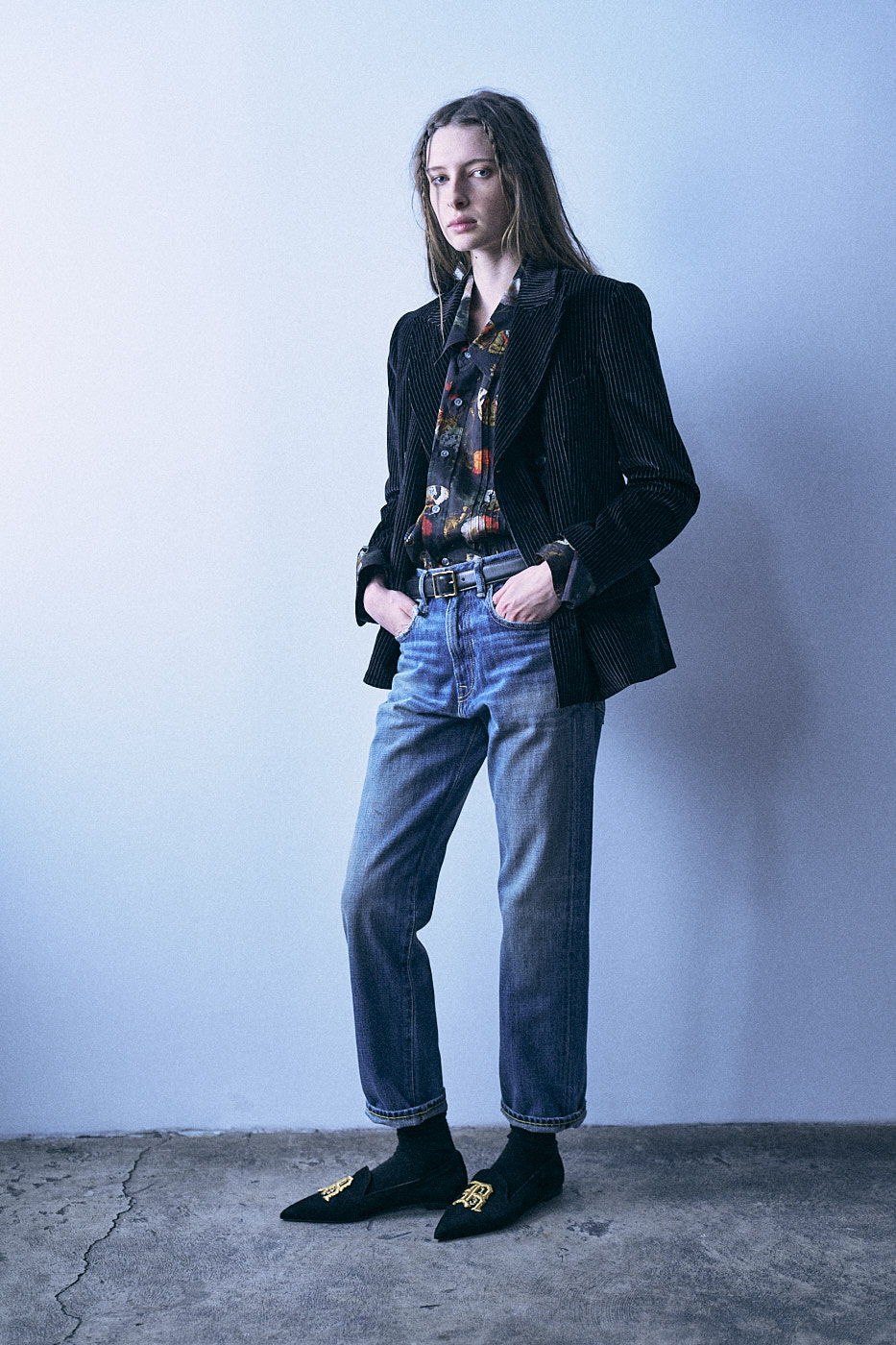 Person in a stylish outfit stands against a blue wall.