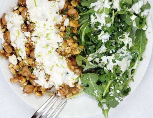 Bowl with grains, greens, and creamy dressing on a white background.