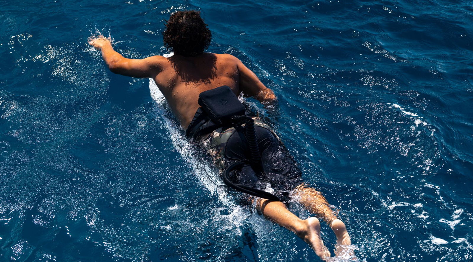 Person swimming on a surfboard in deep blue water.
