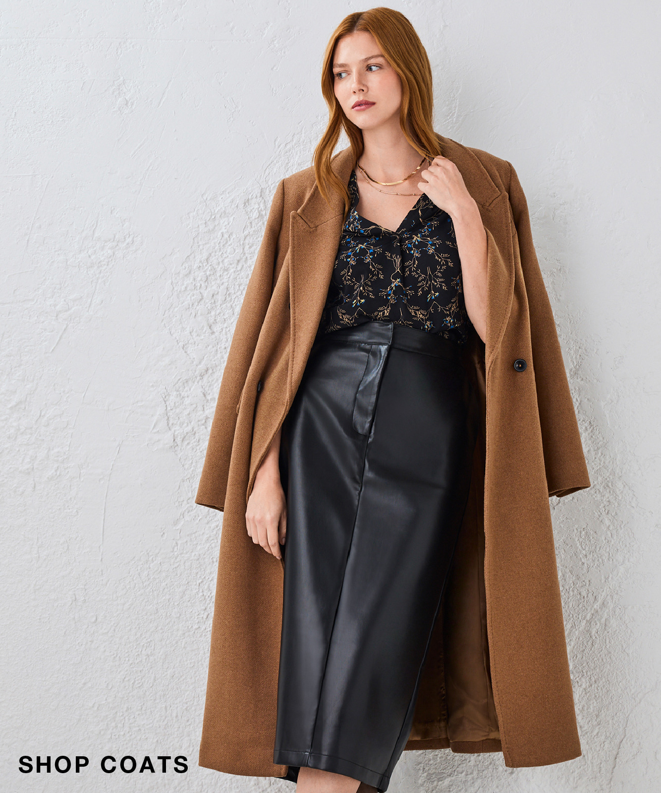 Woman wearing a brown coat and black skirt against a light background.