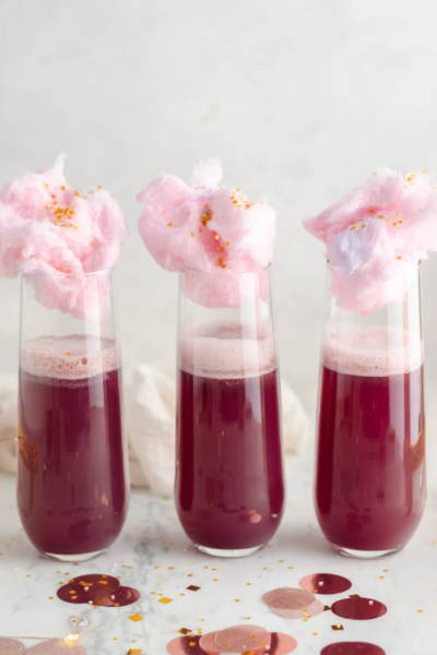 Three pomegranate mocktails in stemless flutes, topped with pink cotton candy and sprinkles.