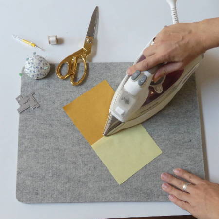 women ironing a piece of a quilt block with a hot iron on a wool pressing mat