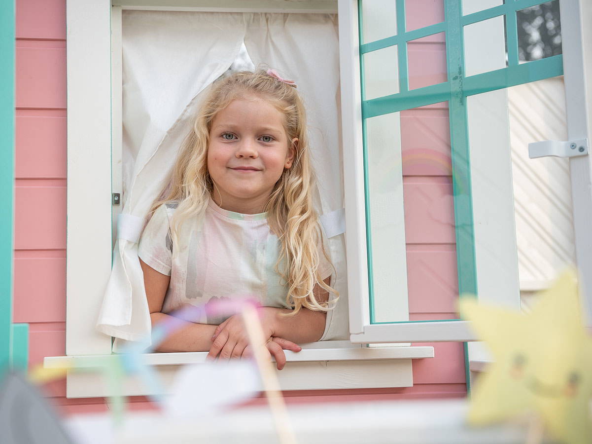  Girl looks out of pink outdoor playhouse window by WholeWoodPlayhouses