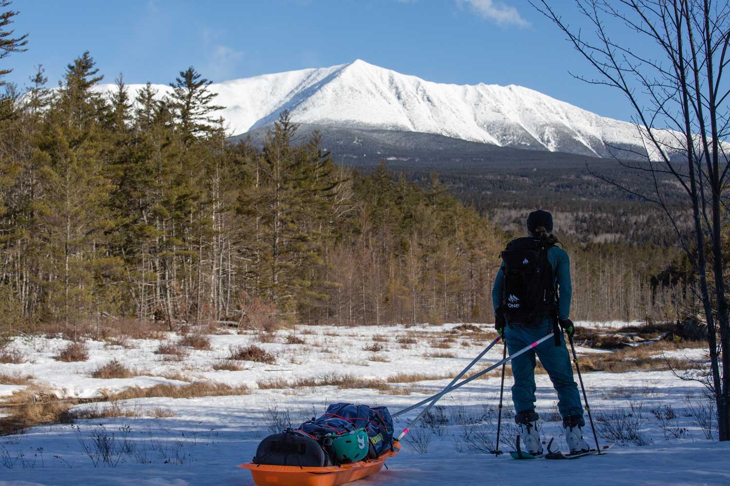 Person splitboarding with sled in snowy landscape, mountains in background.