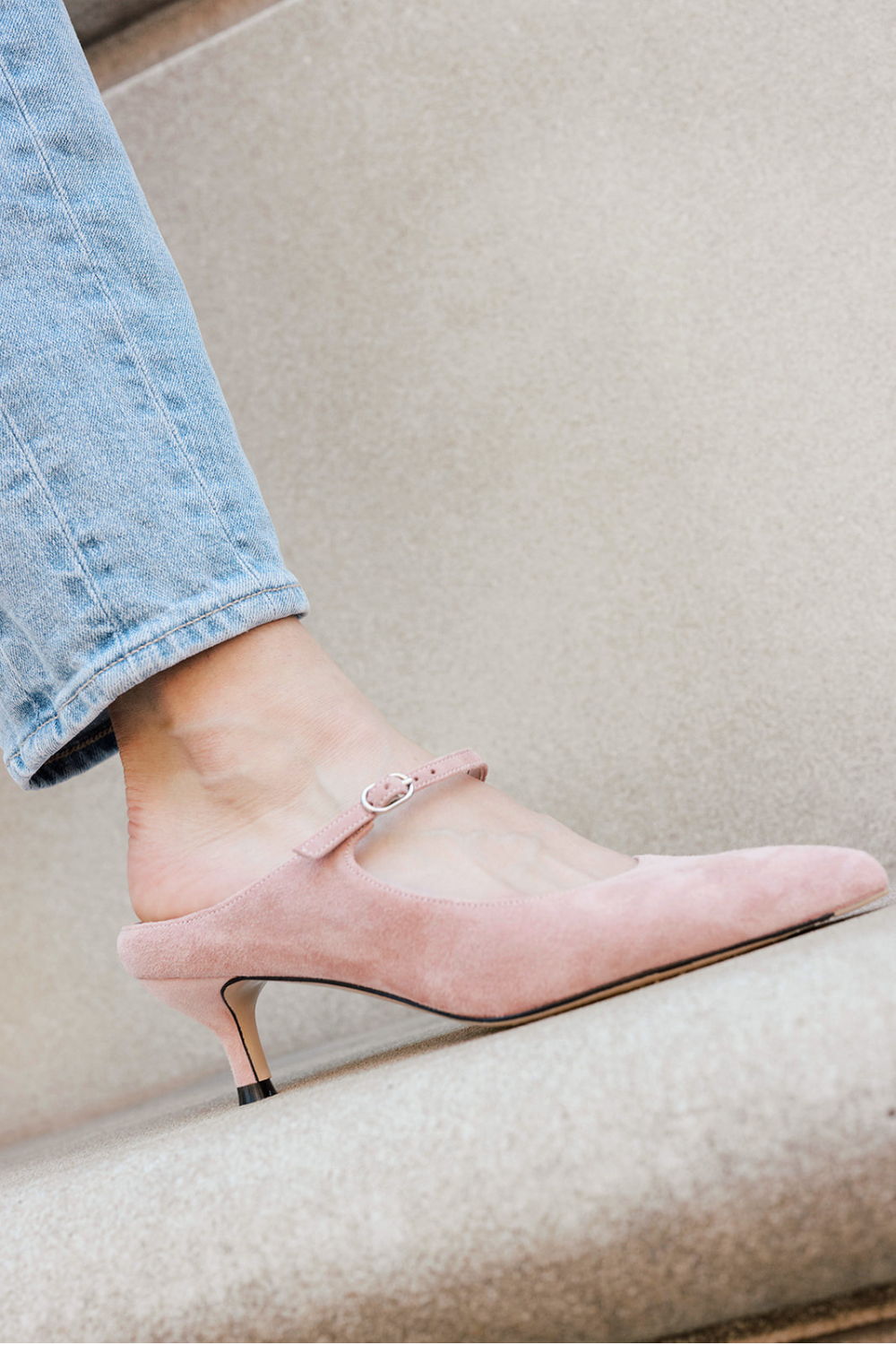 A pink heeled shoe worn with light blue jeans.
