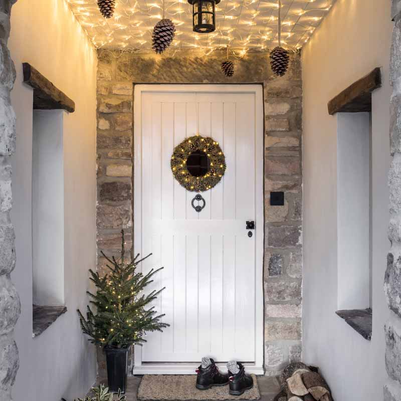 Porch with a wreath and miniature Christmas tree by the doorway.