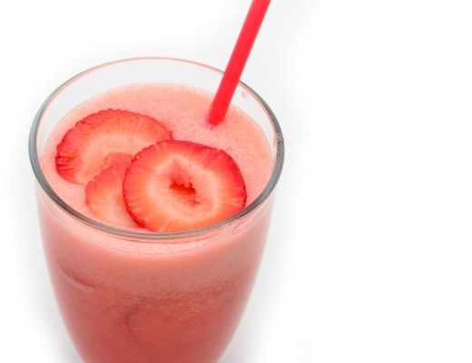 Strawberry smoothie in a glass with a red straw and sliced strawberries.