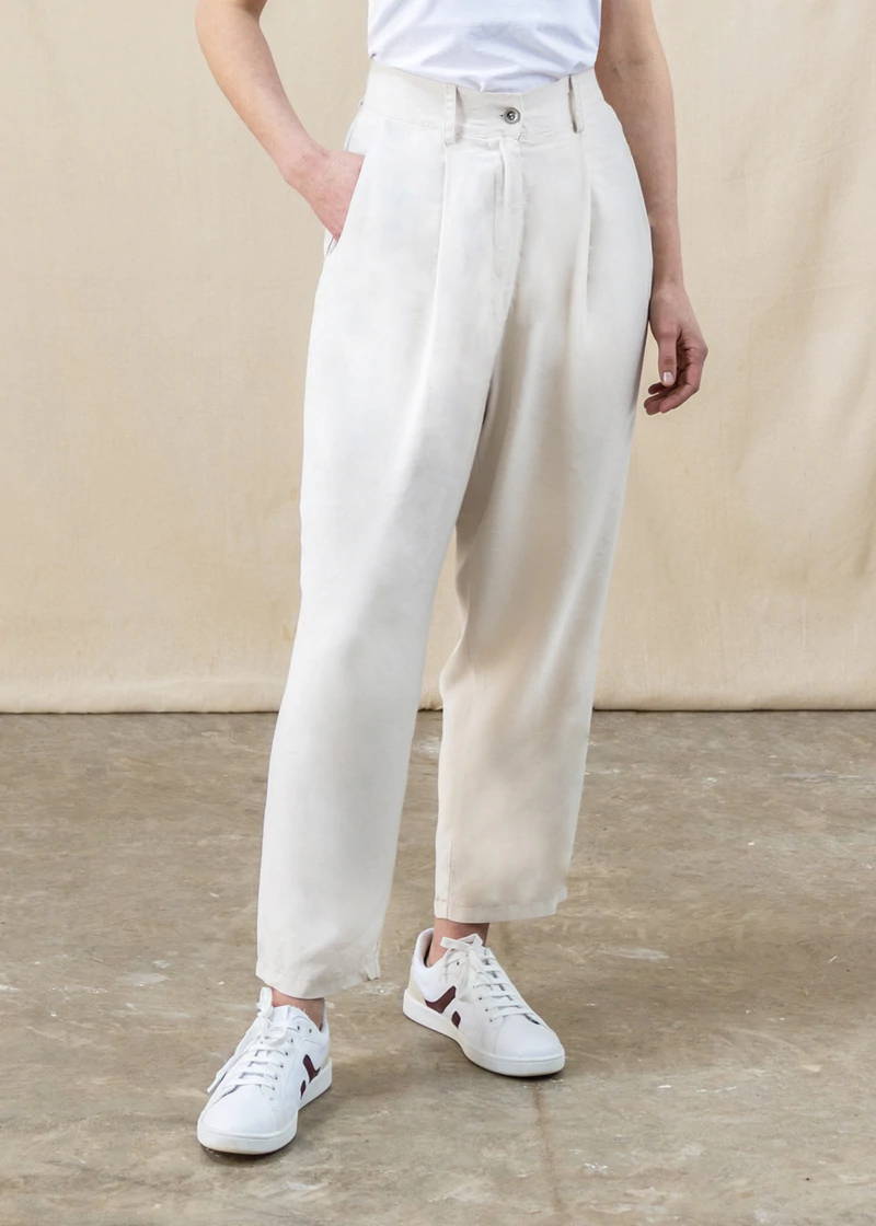 A model wearing cream tailored trousers and trainers