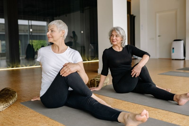 Two women practicing yoga on mats in a bright studio.