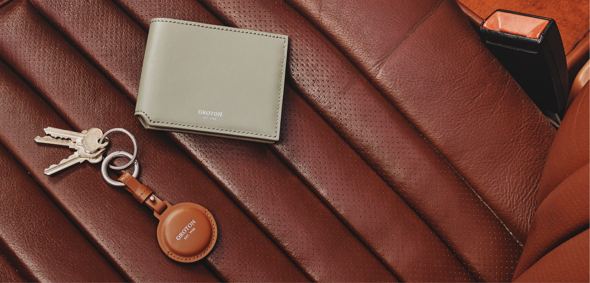 A wallet and keys resting on a brown leather surface.
