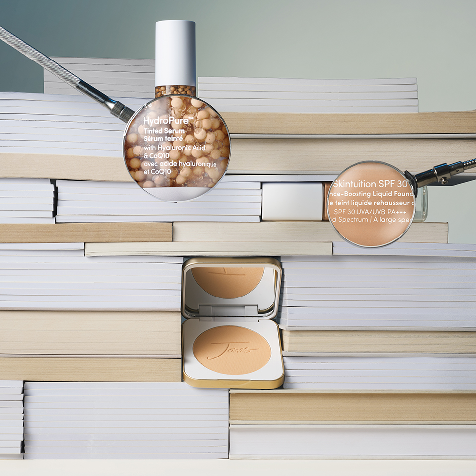 Cosmetics products displayed on stacked books with magnifying glasses.