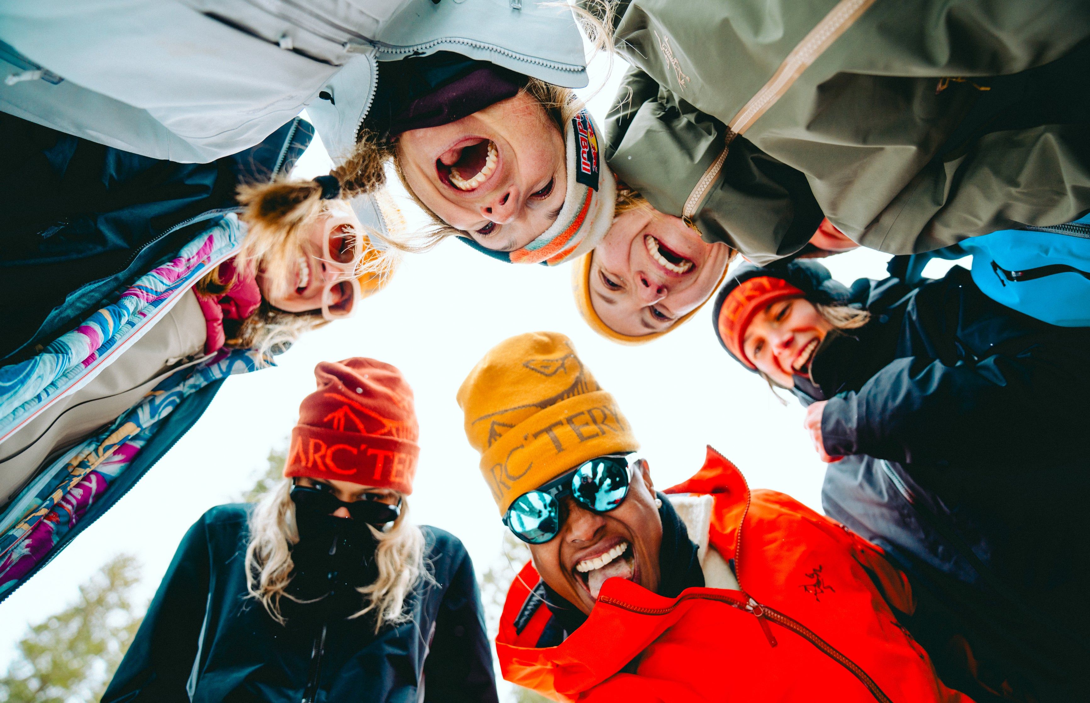 Group of people laughing and posing together outdoors, looking down at the camera.