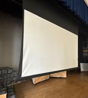 A large, white projection screen mounted in a theater setting.