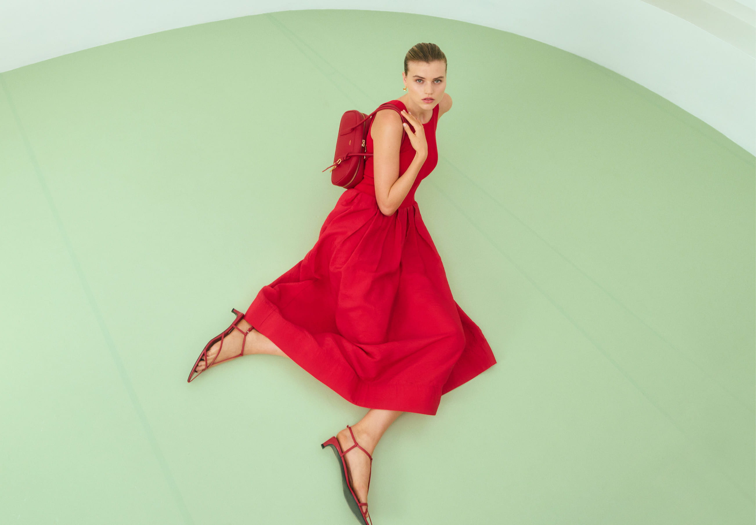 Woman in a red dress poses on a green background.