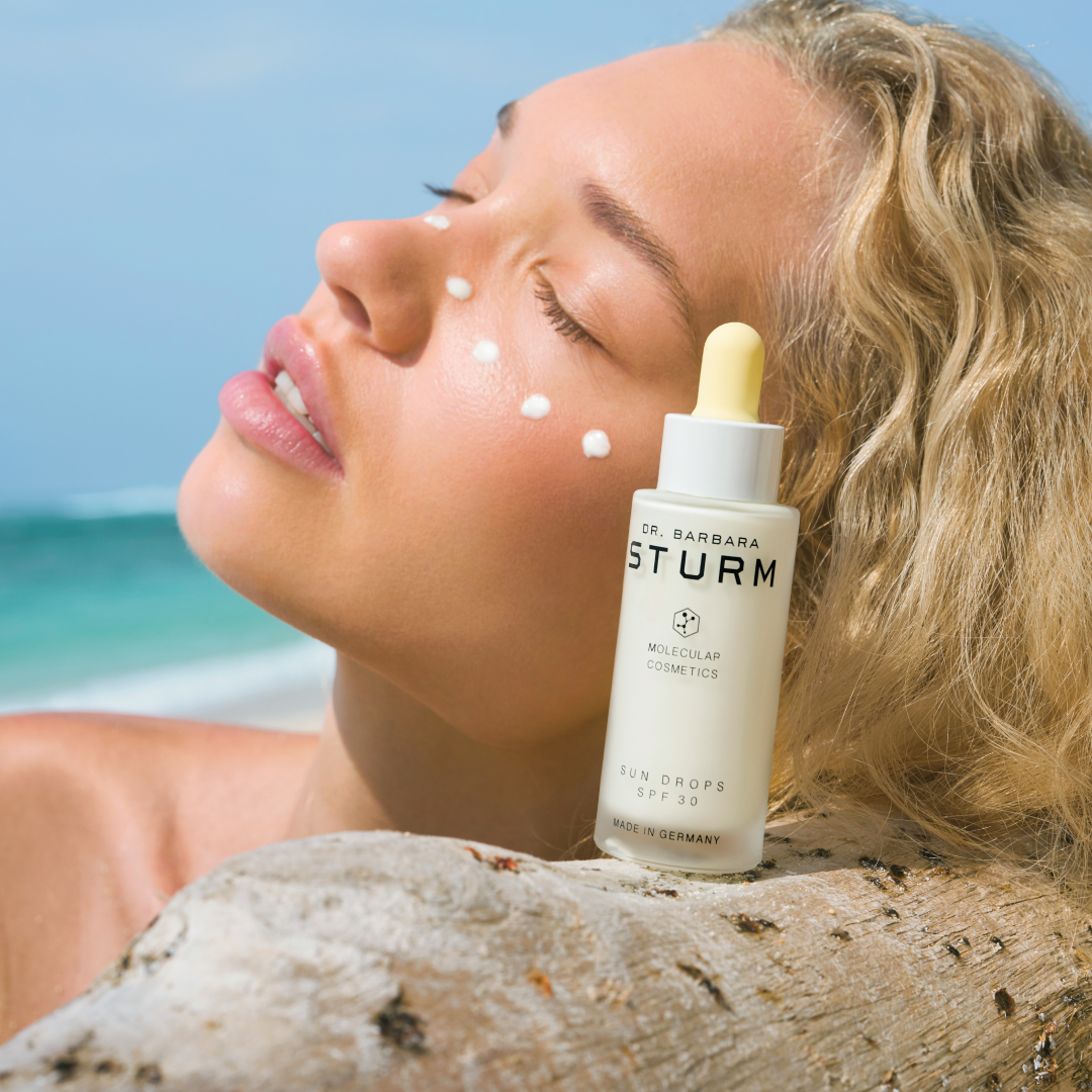 Woman applying skincare product on her face at the beach.