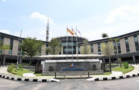 Modern building with flags in front, surrounded by greenery and pavement.