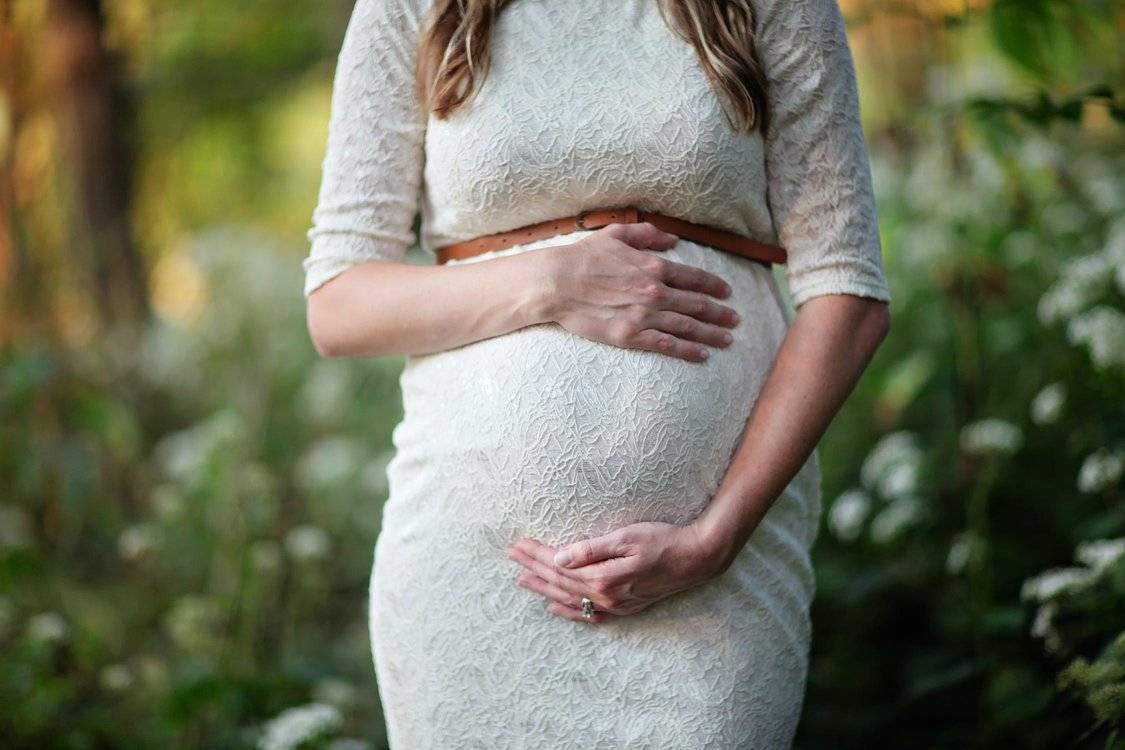 Pregnant Woman In White Dress Holding Stomach With Both Hands