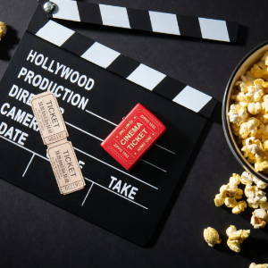Lifestyle image of Cinema Ticket Red Matte Windproof Lighter laying on a movie clapperboard with popcorn scattered around it