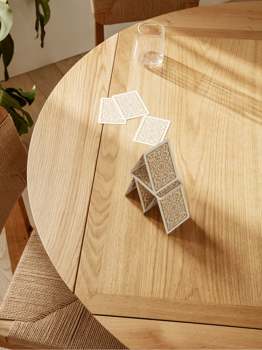 A house of cards on a wooden table B-Table Extendable by Gubi with sunlight.