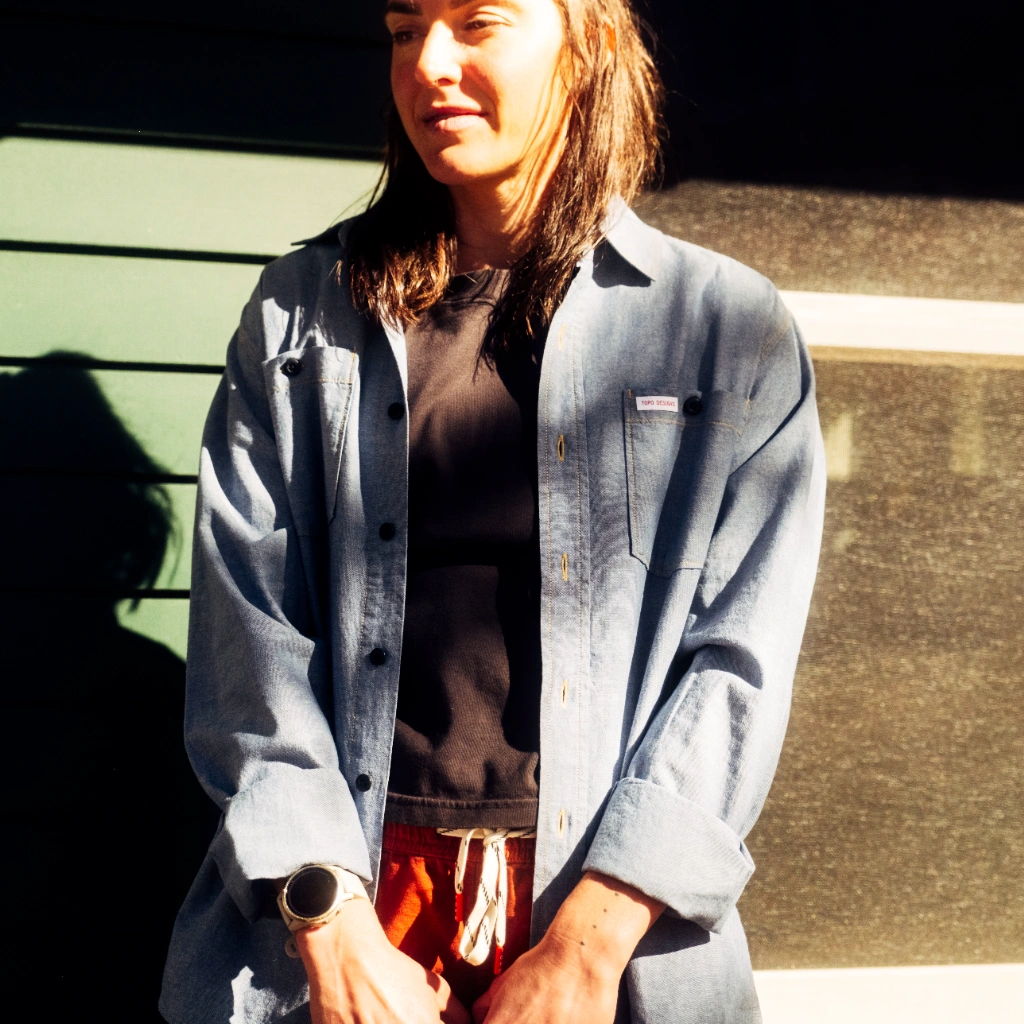 Person standing in sunlight wearing a denim shirt and shorts.