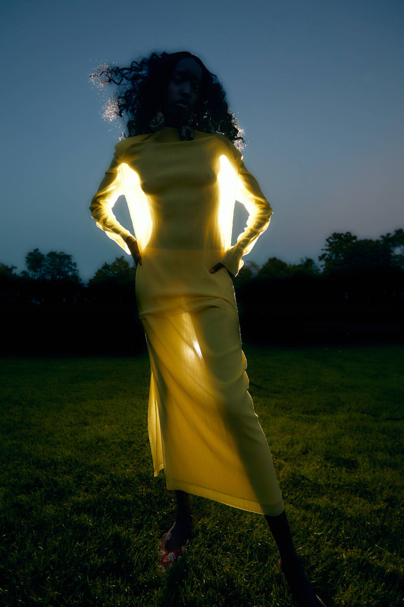 Silhouette of a person in a glowing yellow dress at dusk.