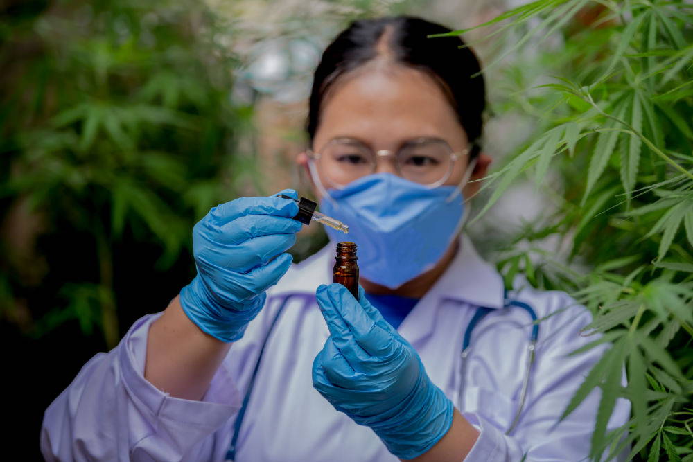 A scientist holding a bottle of CBD oil in a greenhouse