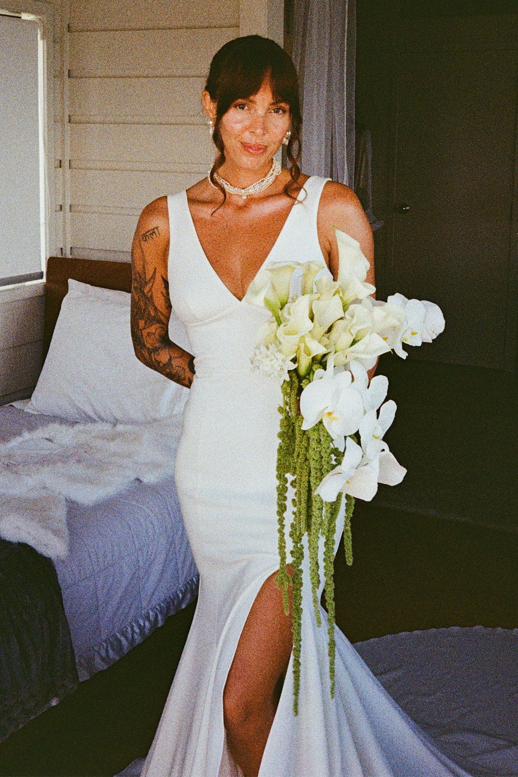 Bride in a white dress holding a bouquet, standing in a room.