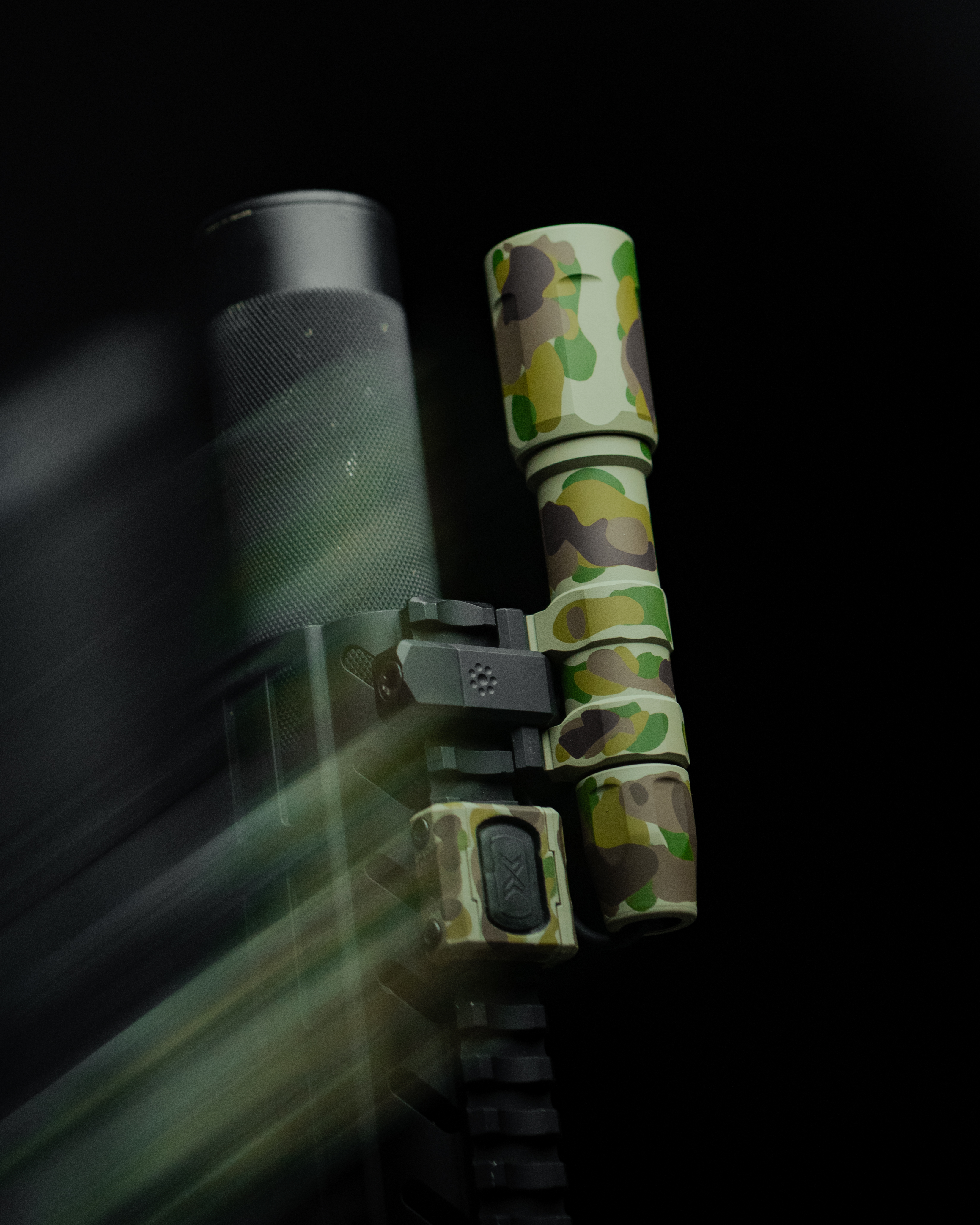 Close-up of a camouflaged firearm attachment against a dark background.