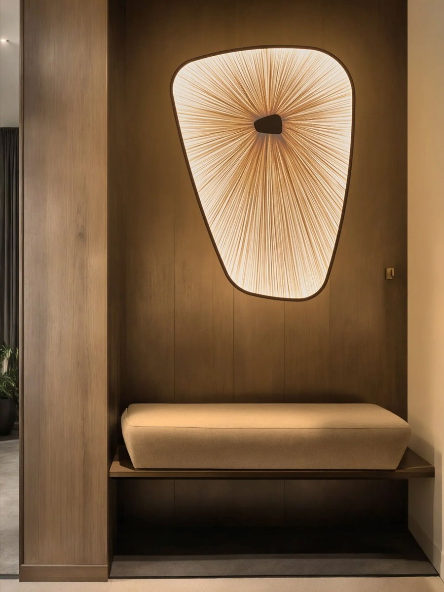 Modern wall design with a unique light fixture and a wooden bench.