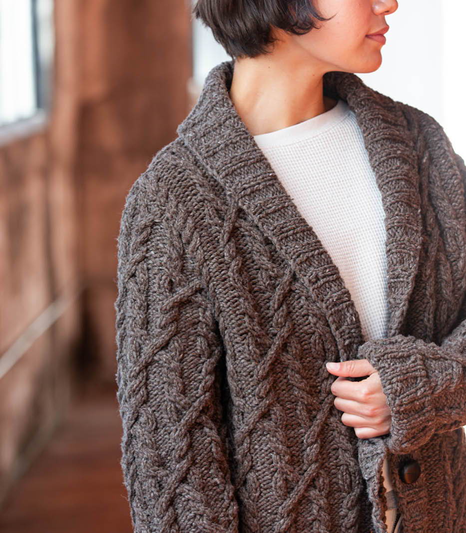 Front, side sleeve view of a female model wearing a hand knit all-over cable cardigan.