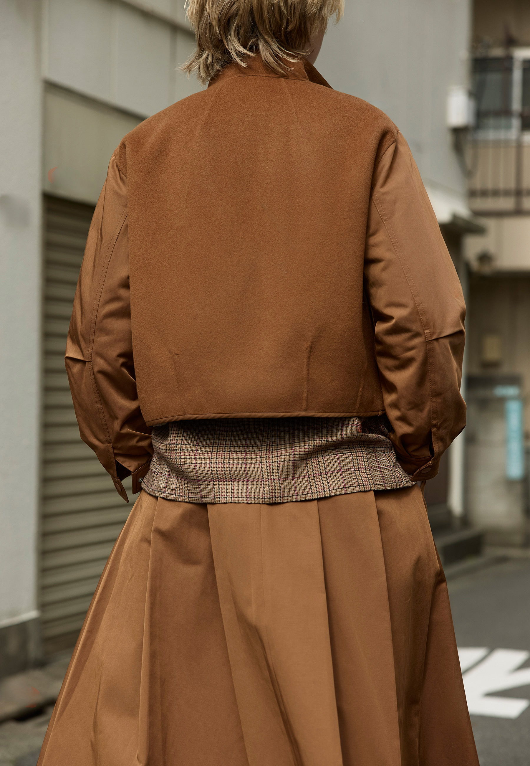 Person wearing a brown jacket and skirt, viewed from the back.