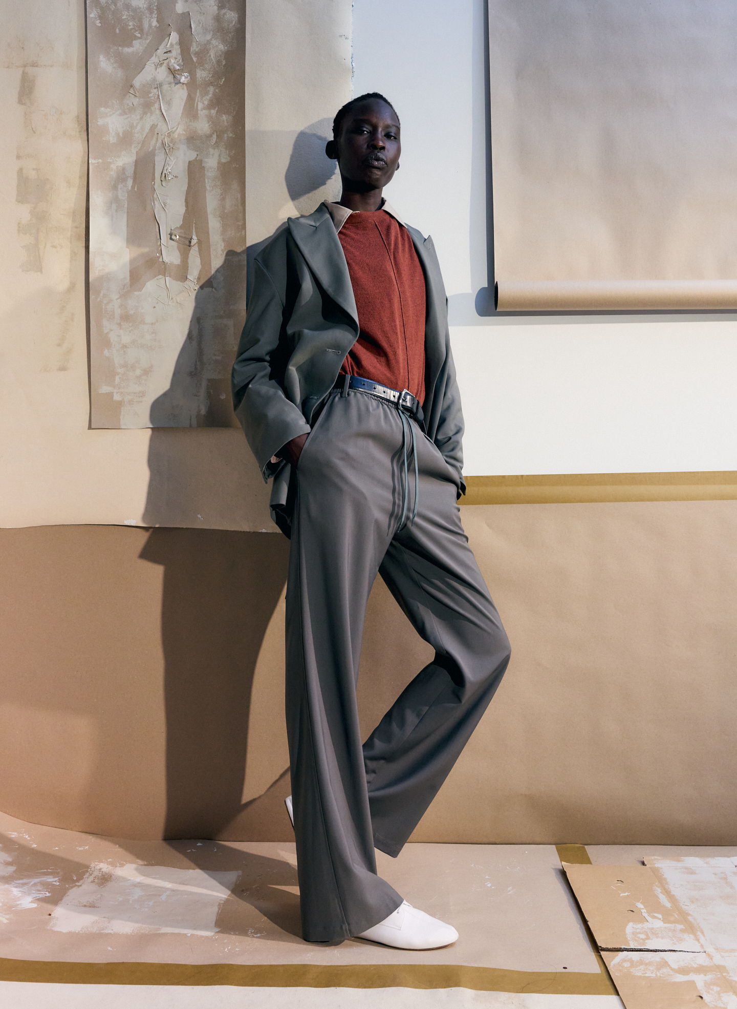 A person in a stylish suit poses against a minimalist backdrop.