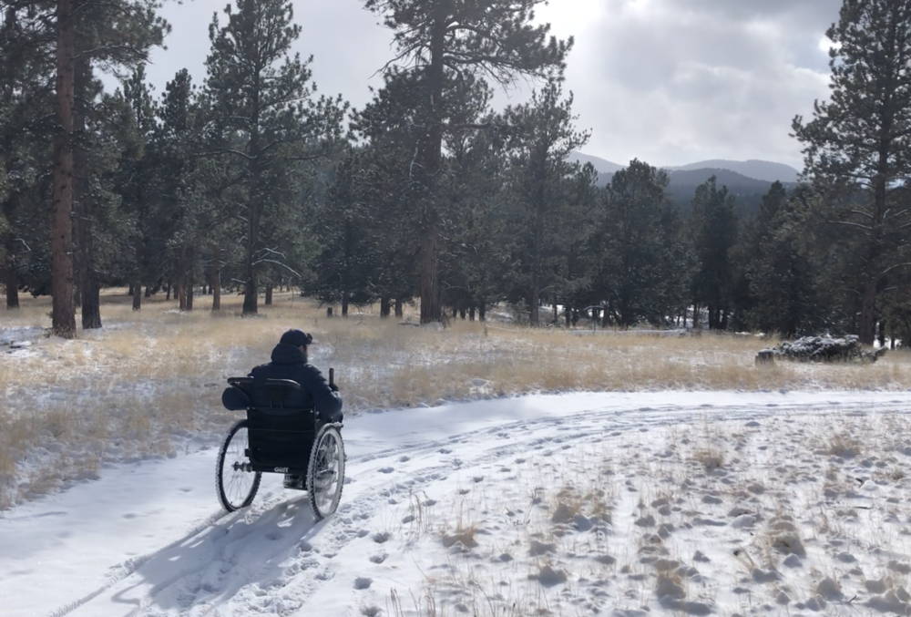 Person riding GRIT Freedom Chair on snowy trail in forest area
