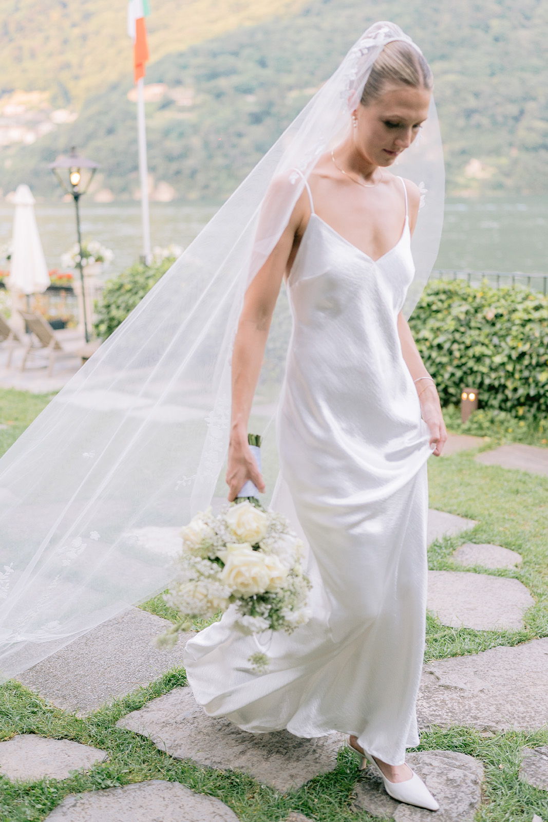 Bride in a white dress and veil, holding a bouquet, walking outdoors.
