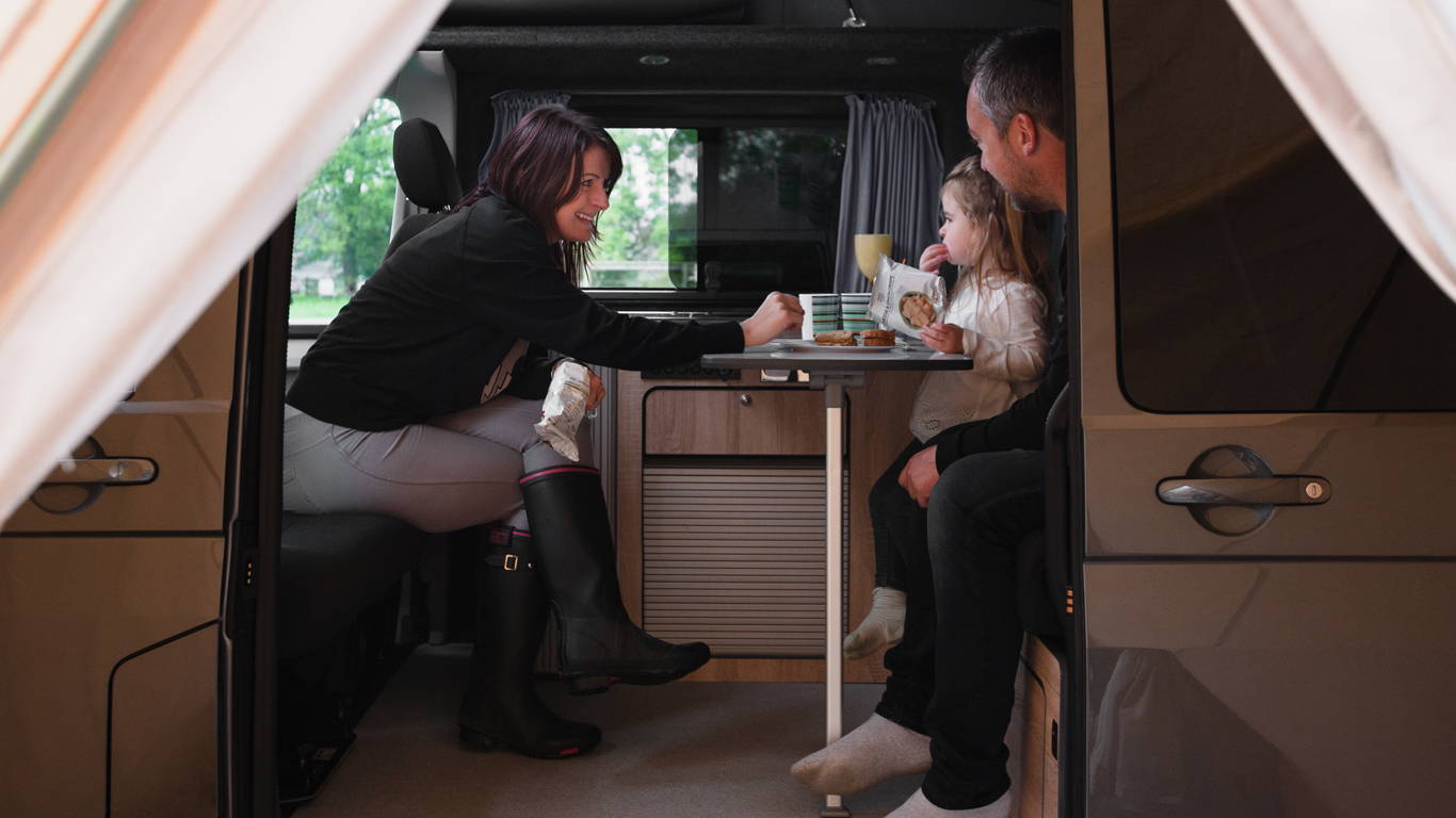 Photo of Sarah, James, and Tilly sat in a camper van
