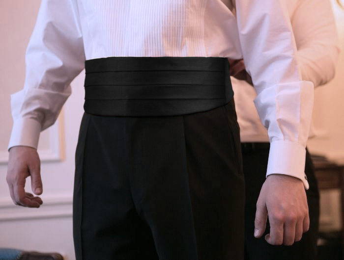 Man getting help putting on a cummerbund in formal attire