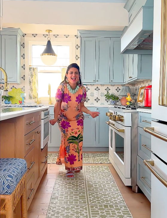 A woman in a colorful dress stands in a bright kitchen.