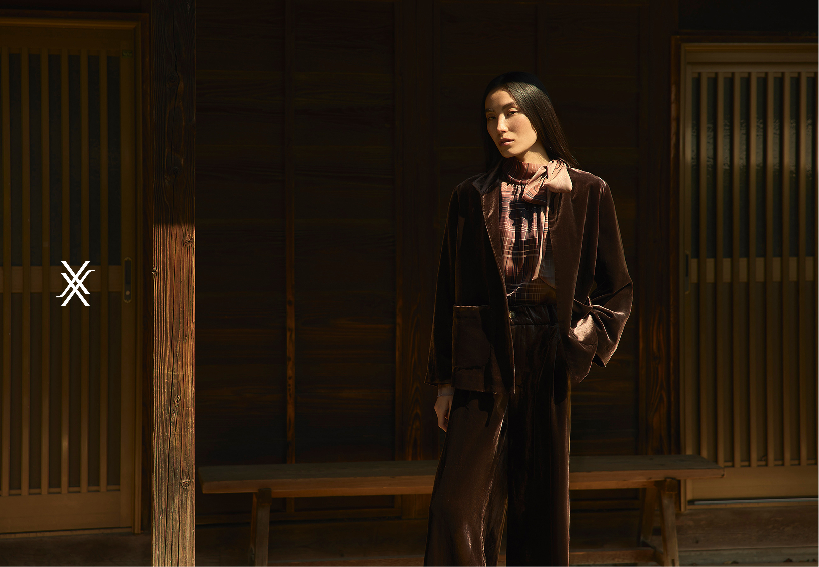 Person in stylish outfit stands in a dimly lit room with wooden accents.